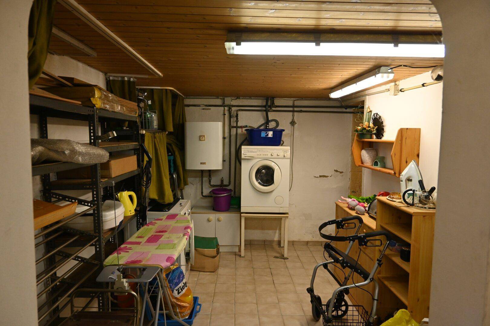 Waschküche im Keller mit Waschmaschine, Boiler und Regalen für zusätzlichen Stauraum.
