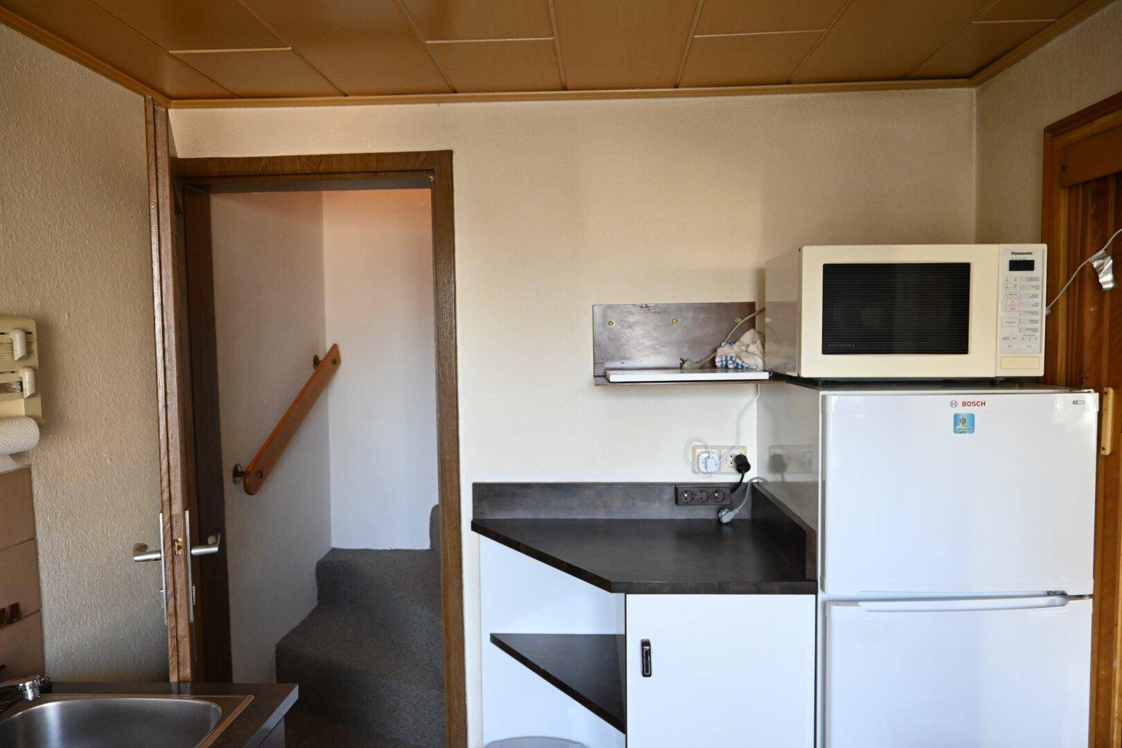 Kleine Küchenzeile mit Mikrowelle, Kühlschrank und Spüle, ideal für eine Einliegerwohnung.