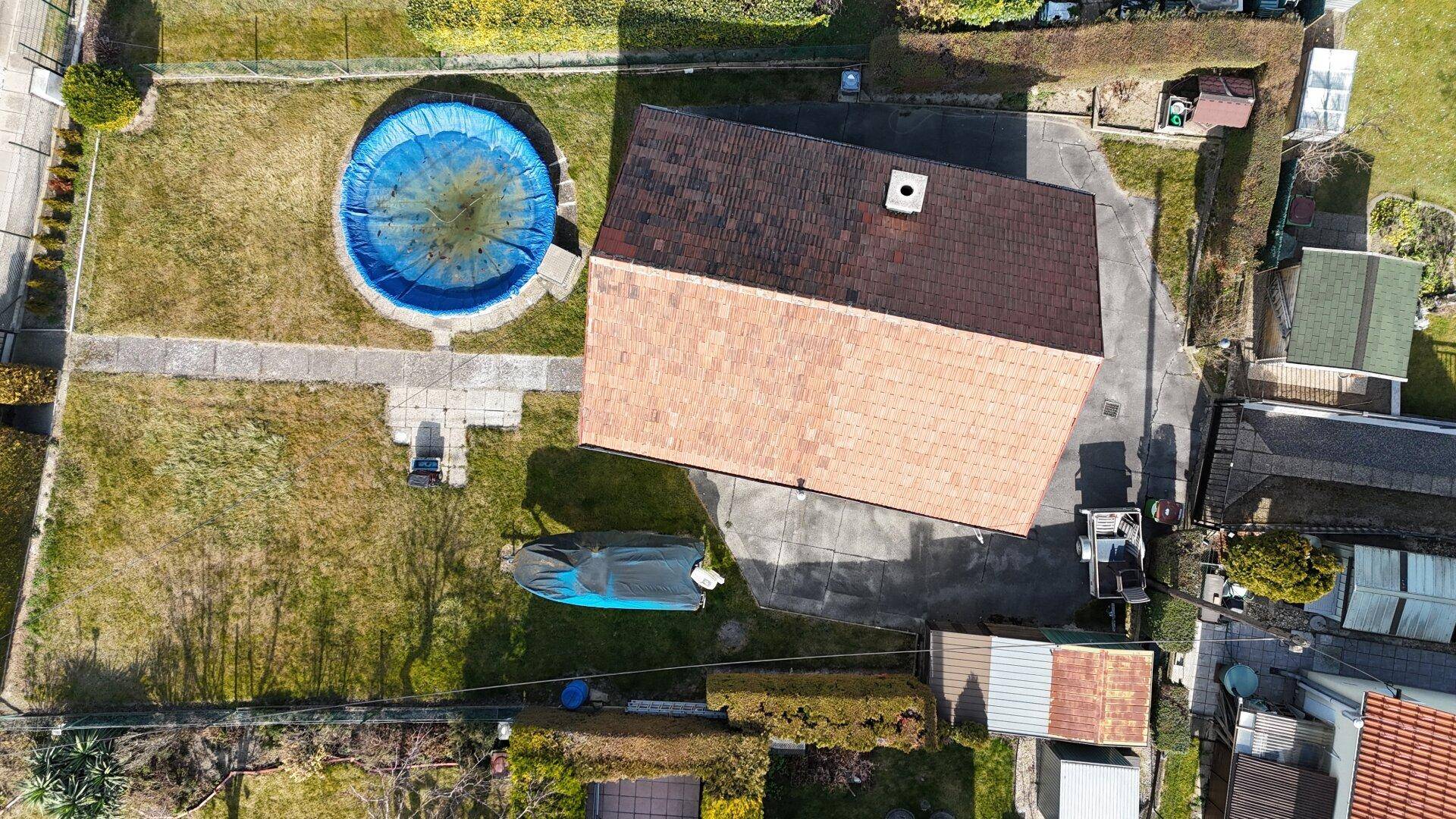 Luftaufnahme des Grundstücks mit Haus, Garten, Pool und umliegender Bebauung.