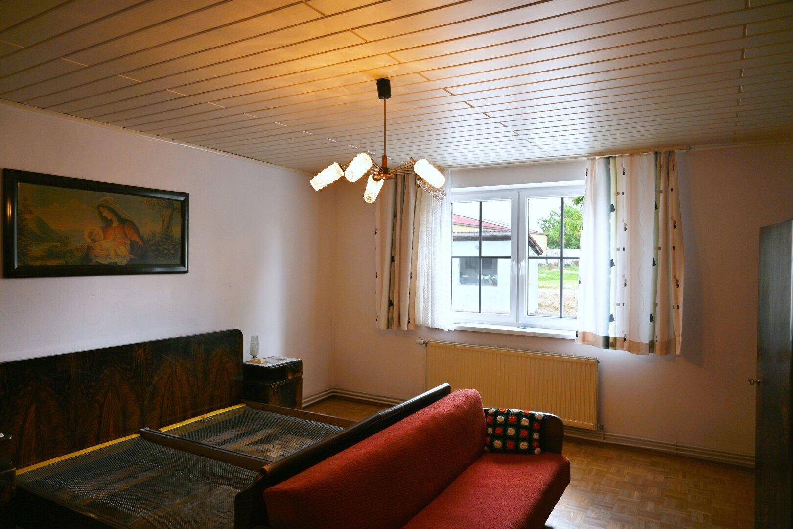 Schlafzimmer mit Doppelbett, rotem Sofa und Holzdecke.