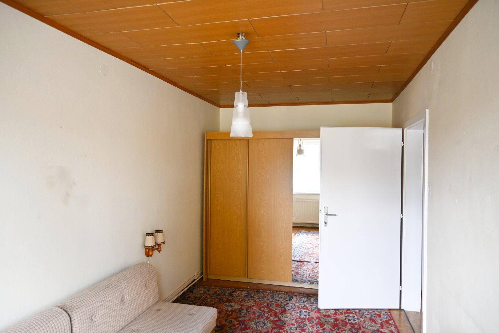 Schlafzimmer mit Teppichboden, Schrank und Blick auf den Flur.