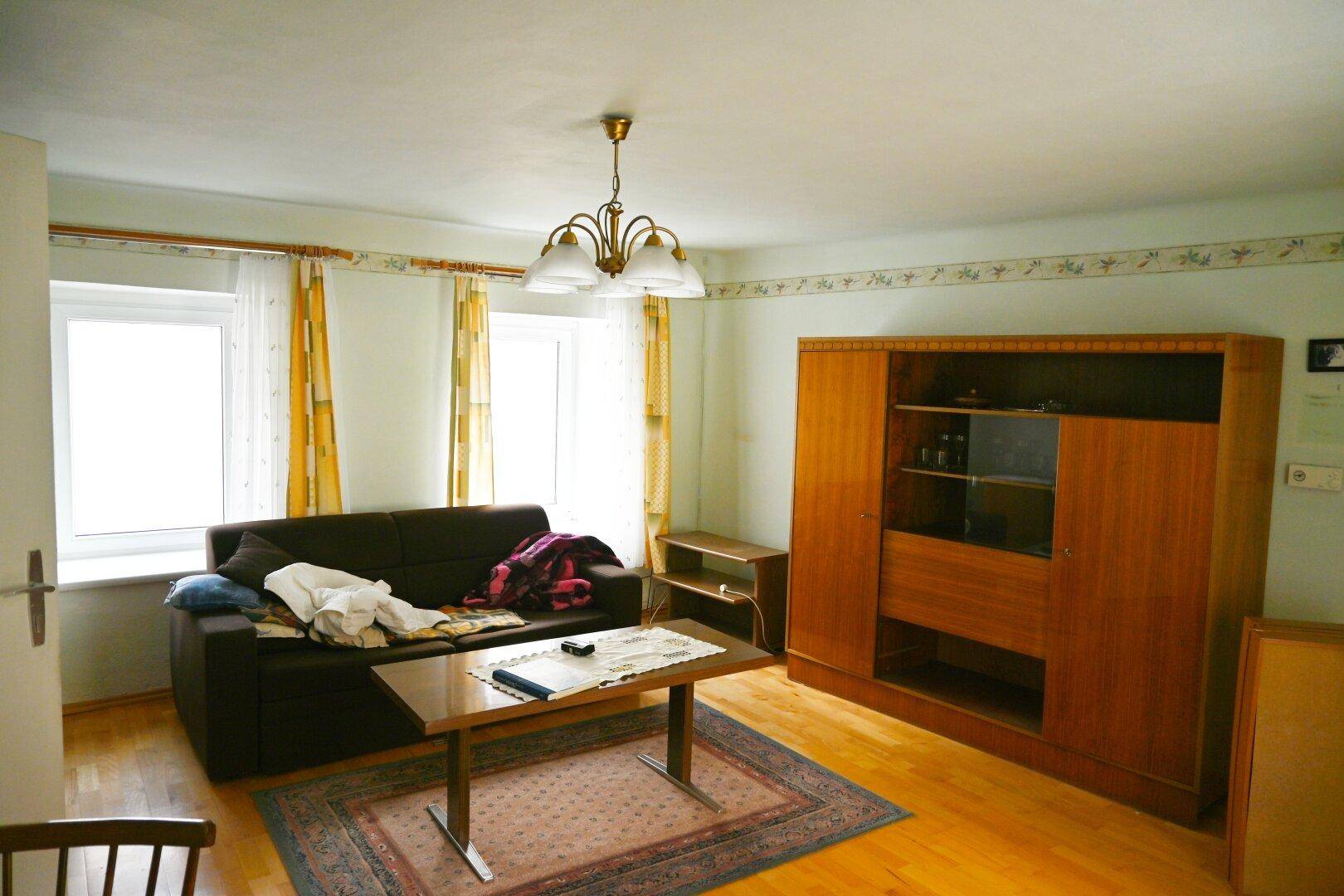 Gemütliches Wohnzimmer mit Holzboden, dunklem Sofa und traditionellen Möbeln.
