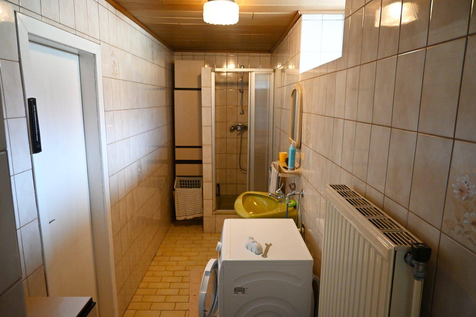 Gefliestes Badezimmer mit Duschkabine, Waschmaschine und gelbem Waschbecken.
