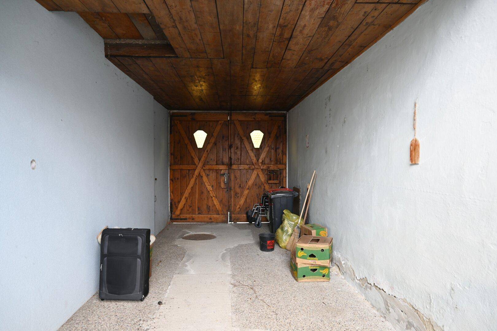 Überdachter Durchgang mit Holztor und Lagerfläche, führt zu weiteren Gebäuden.