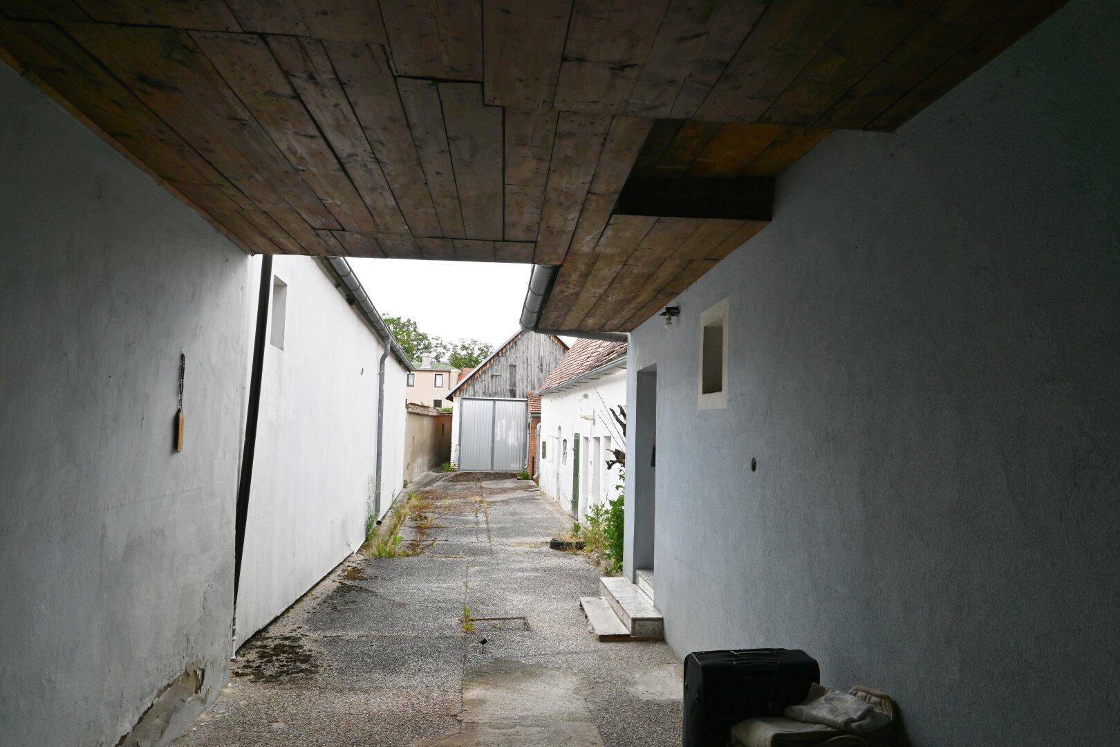 Langer, schmaler Durchgang zwischen Gebäuden mit Betonboden und Blick in den Hof.