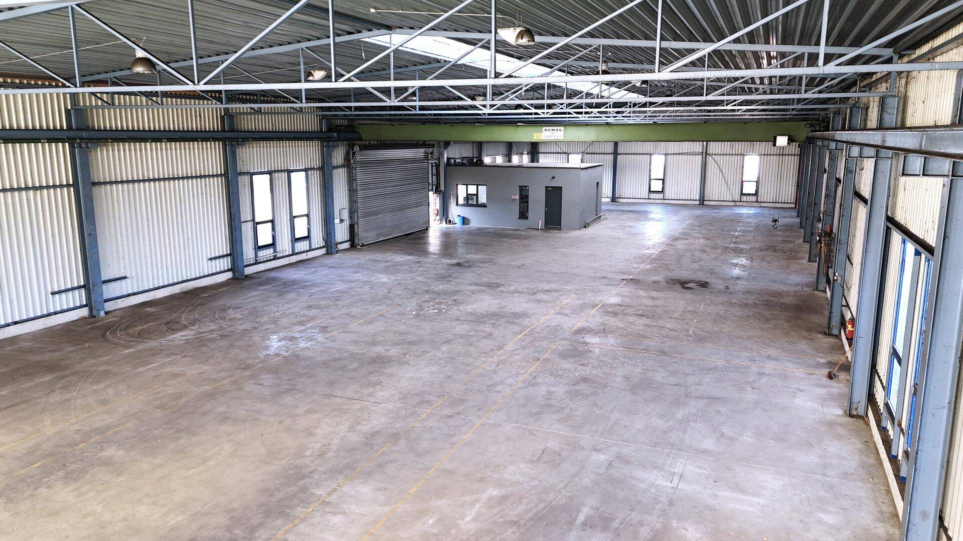 Große Lagerhalle mit Betonboden, hohen Decken und Oberlichtern, ideal für Logistik und Lagerung.