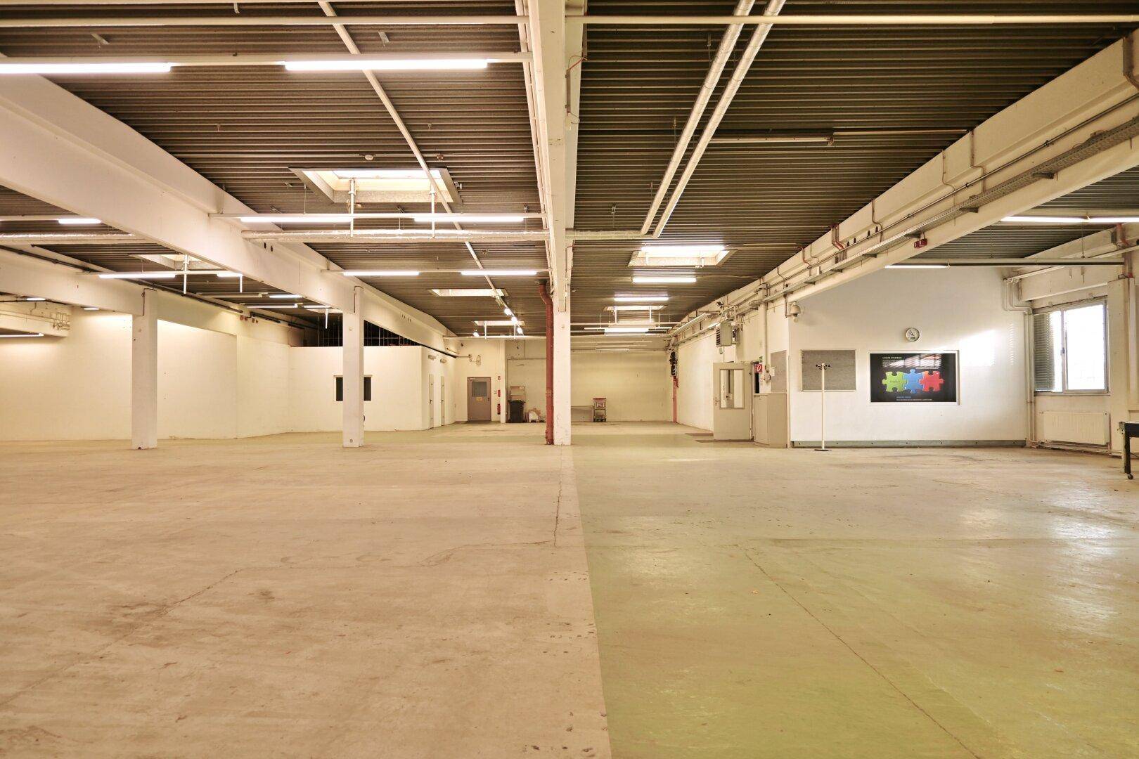 Weitläufige Lagerhalle mit Betonboden, hohen Decken und industrieller Beleuchtung, ideal für große Mengen.