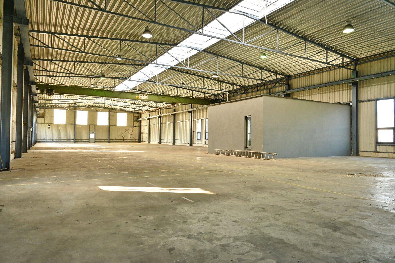 Weitläufige Lagerhalle mit Betonboden, hohen Decken und Oberlichtern, bereit für industrielle Nutzung.