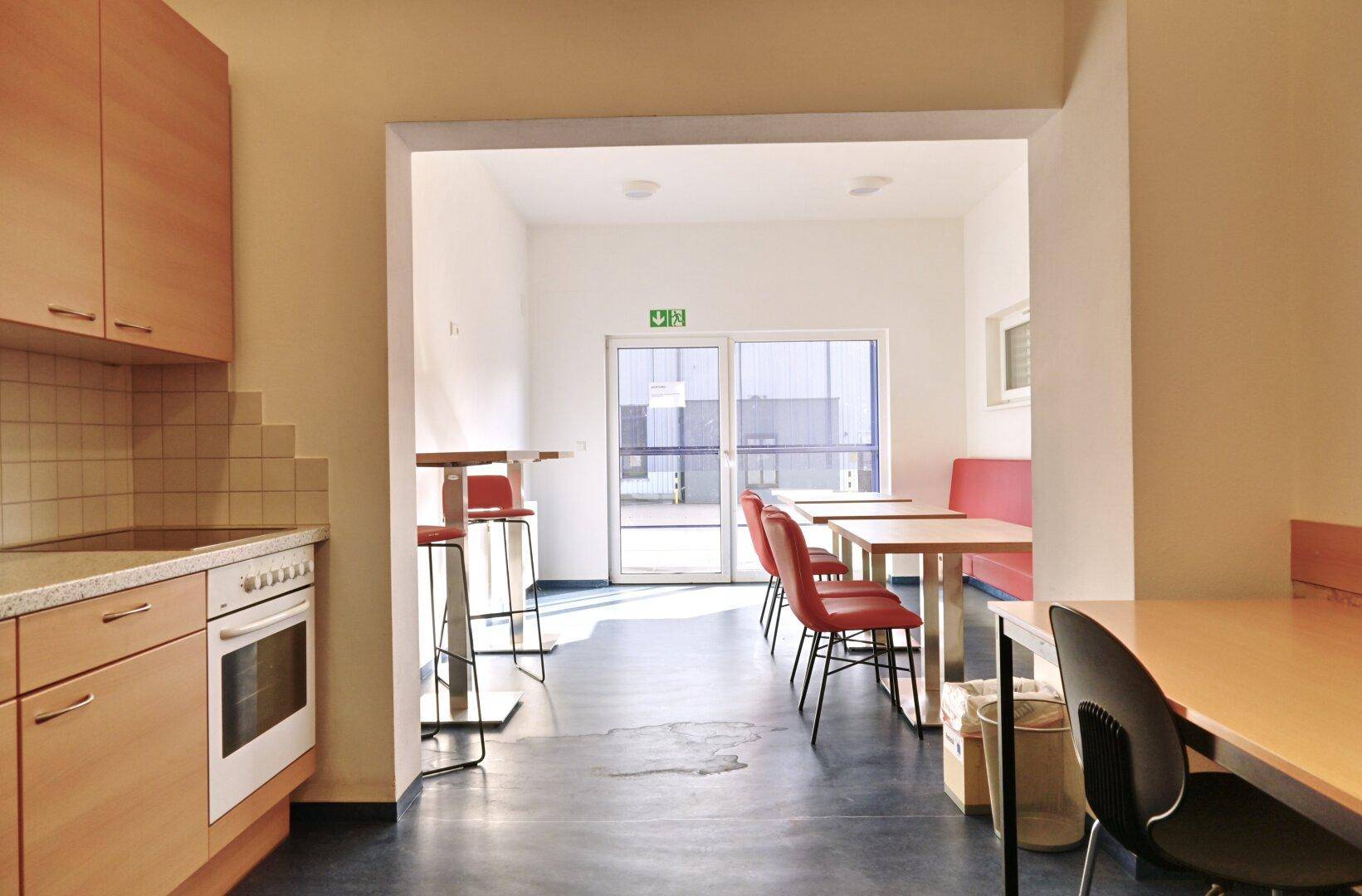 Gemütlicher Pausenraum mit kleiner Küchenzeile, Tischen und Stühlen, ideal für Mitarbeiter.