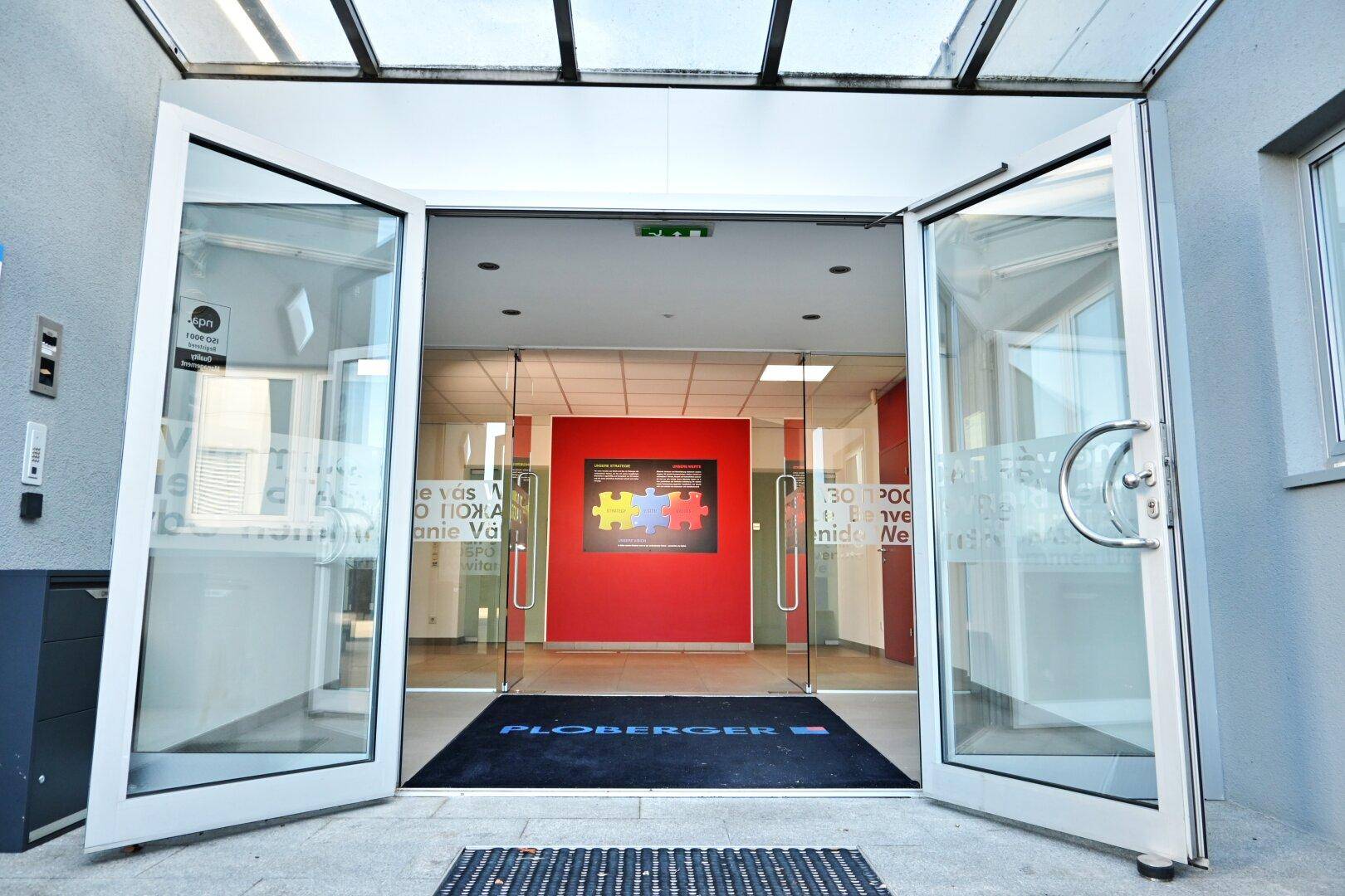 Moderner Eingangsbereich mit Glastüren und Vordach, der zu den Büroräumen des Gebäudes führt.