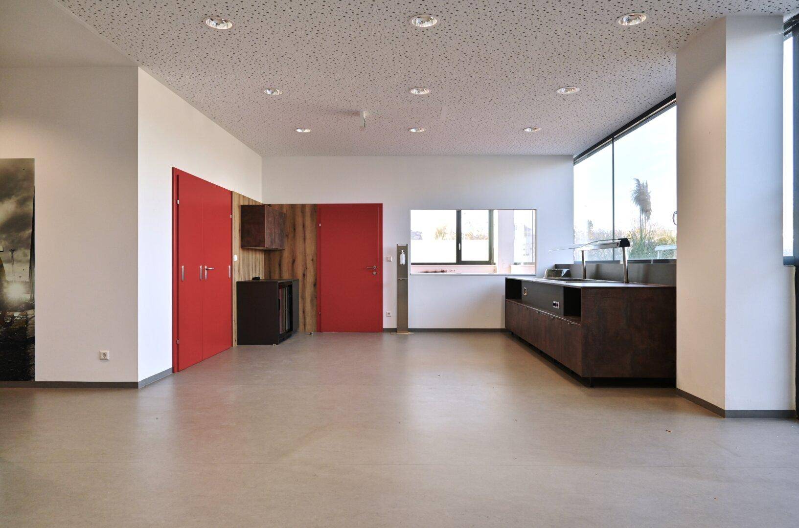 Moderner Bürobereich mit hellem Boden, roten Türen und einer langen Theke, ideal für Empfang oder Kantine.