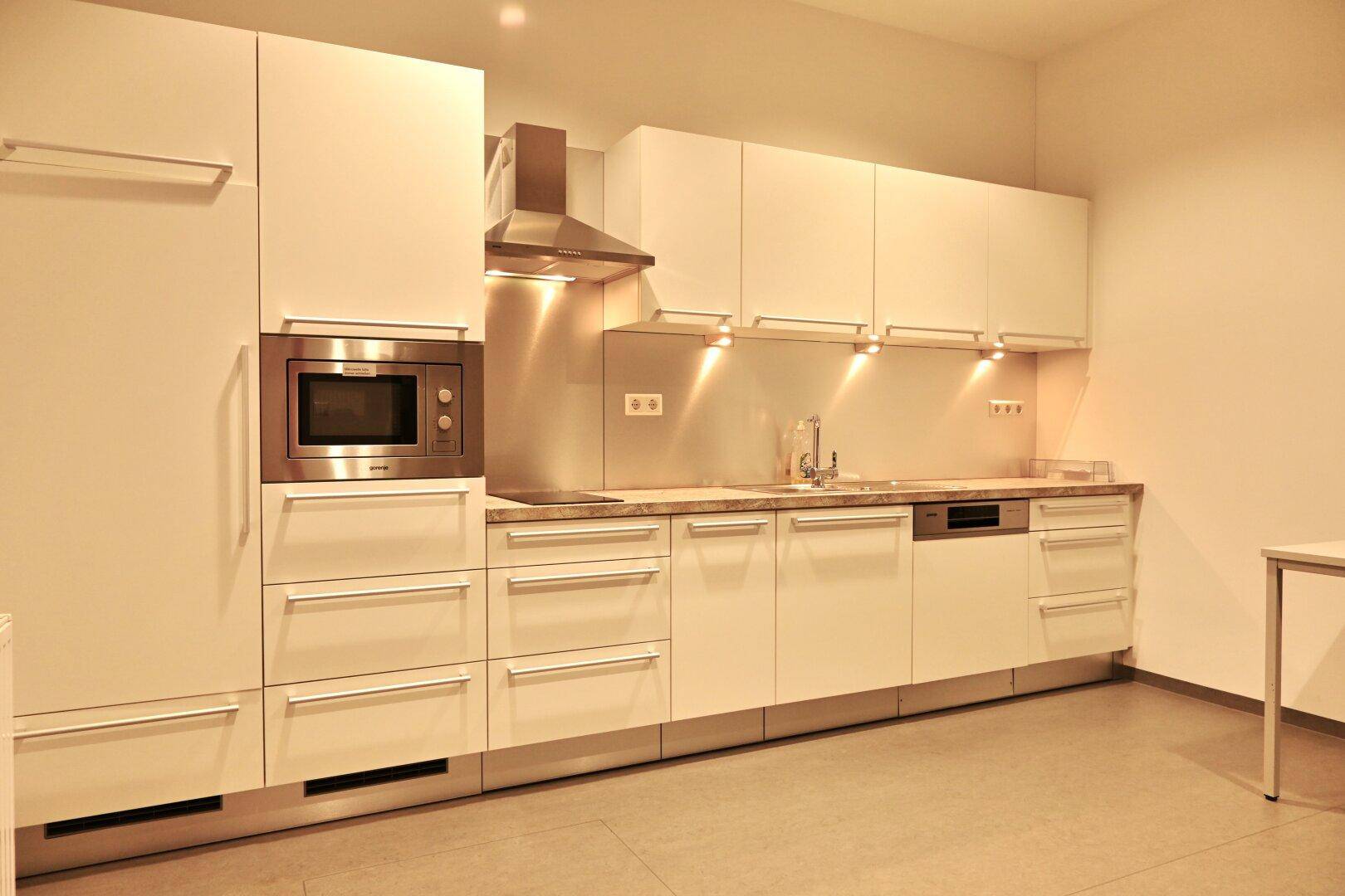 Moderne Einbauküche mit weißen Hochglanzfronten, integrierten Geräten und indirekter Beleuchtung.