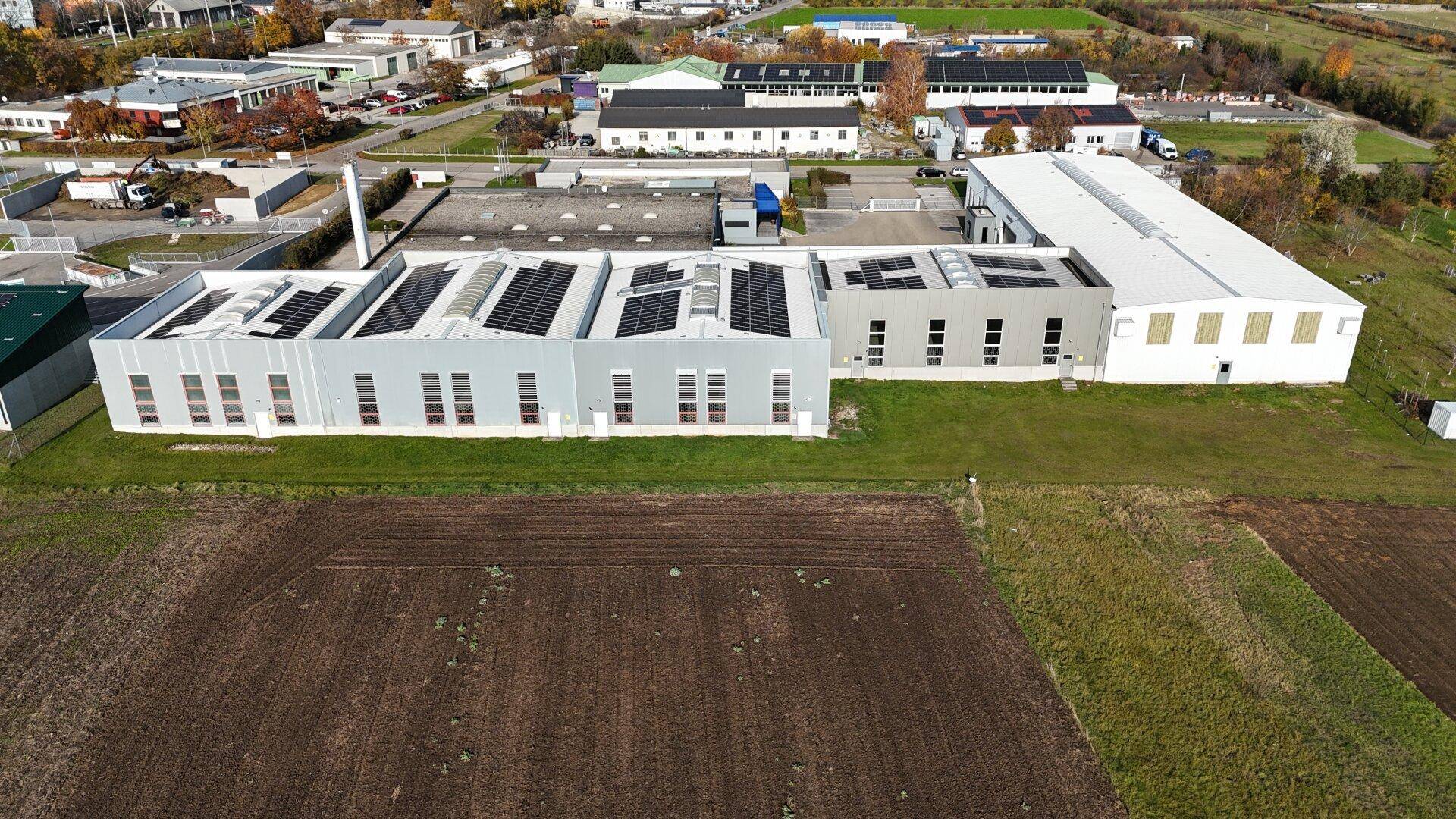 Luftaufnahme eines modernen Gewerbekomplexes mit Photovoltaikanlagen auf den Dächern und umliegenden Feldern.