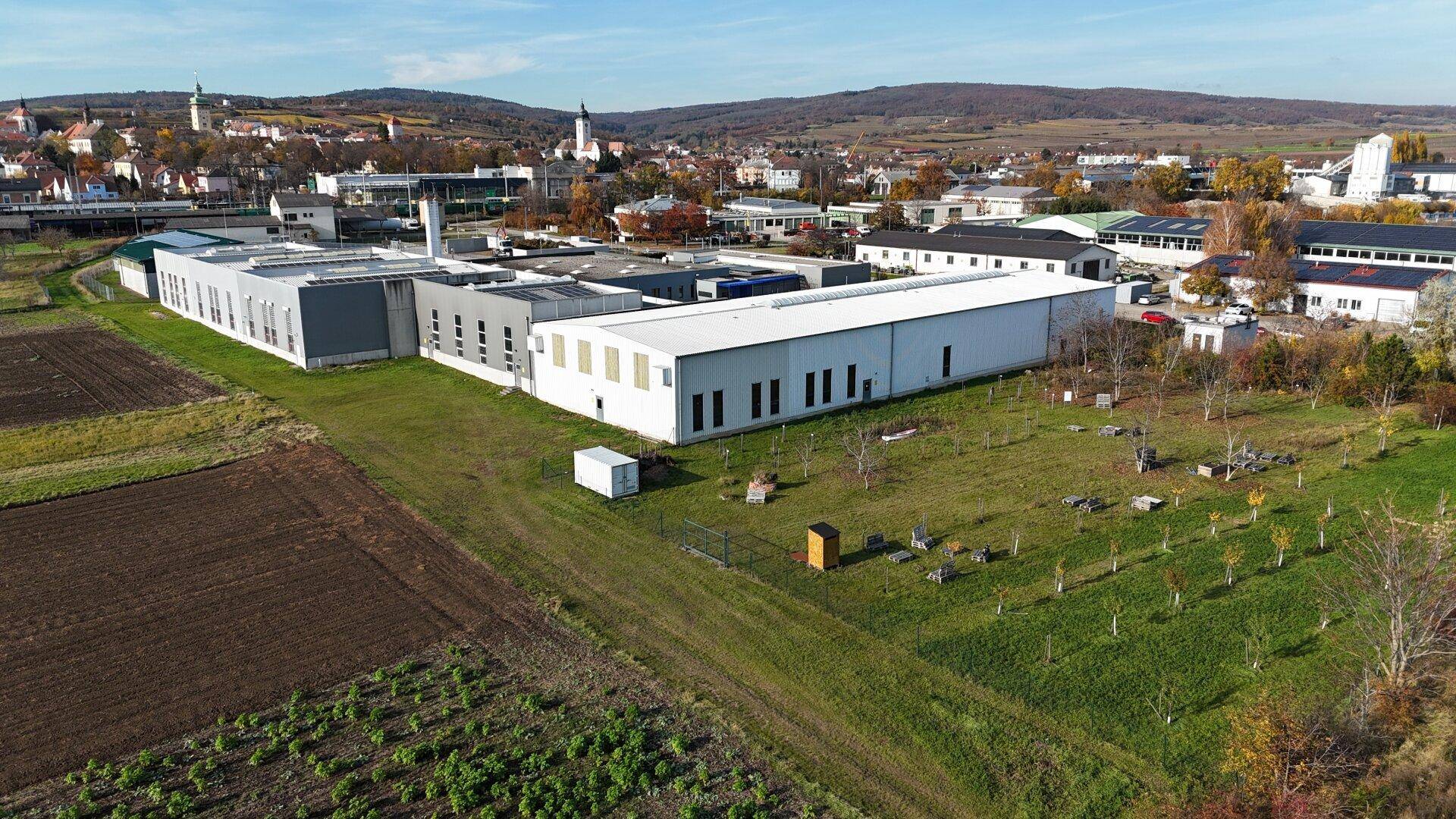 Weitläufiger Gewerbekomplex mit Photovoltaikanlagen, umgeben von Feldern und einer ländlichen Siedlung im Hintergrund.