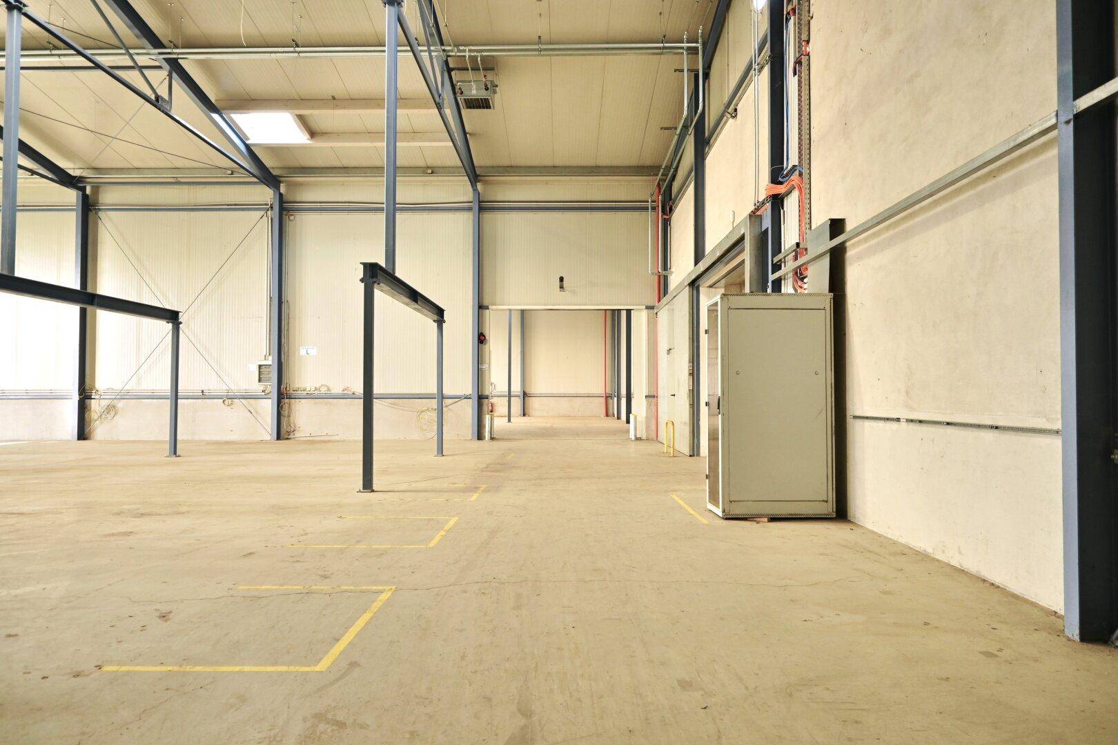 Industrielle Lagerhalle mit Betonboden, hohen Decken und sichtbaren Stahlträgern, die Stabilität bieten.