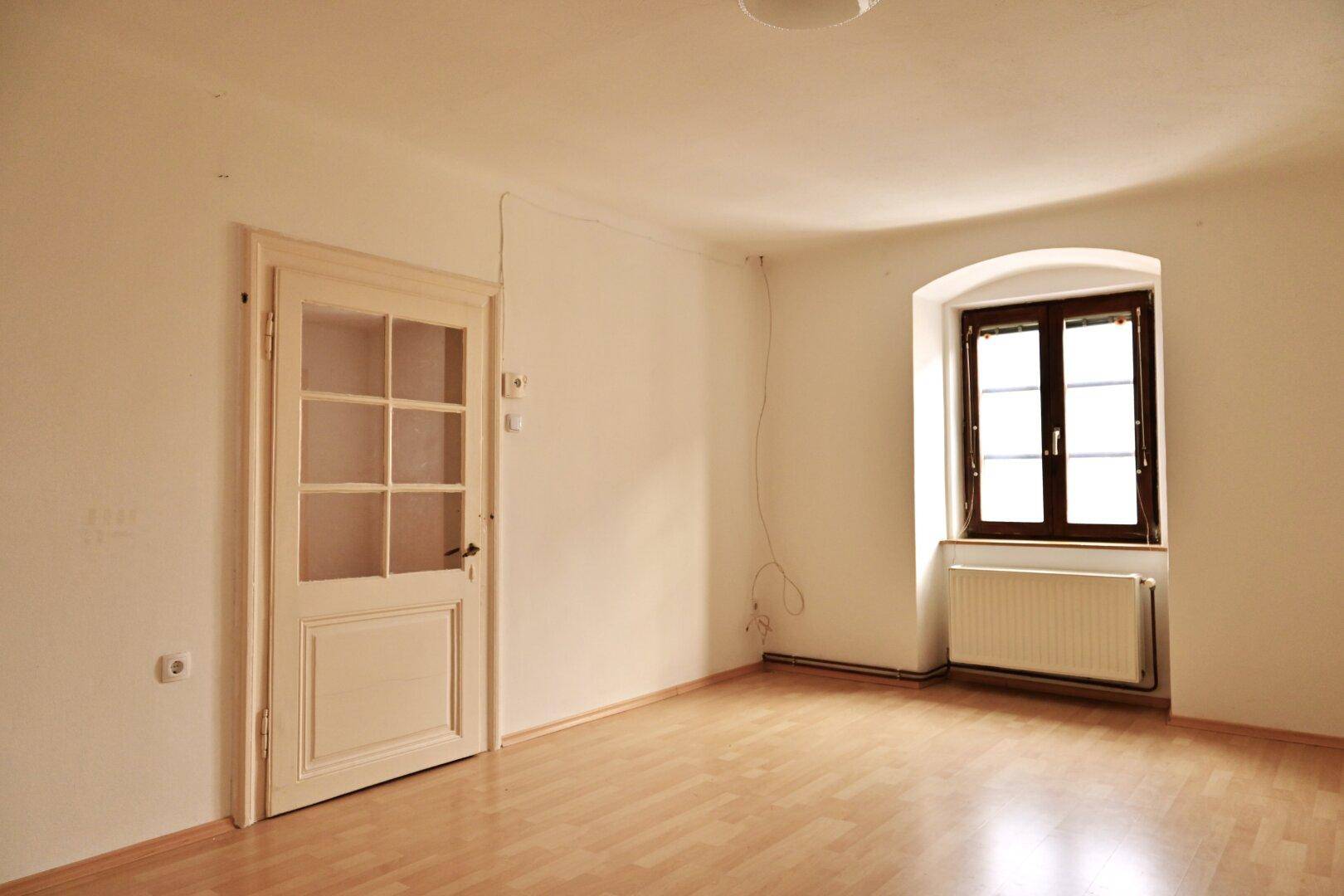 Helles Zimmer mit Holzboden und einer Tür mit Glaseinsätzen, die zu einem anderen Bereich führt.