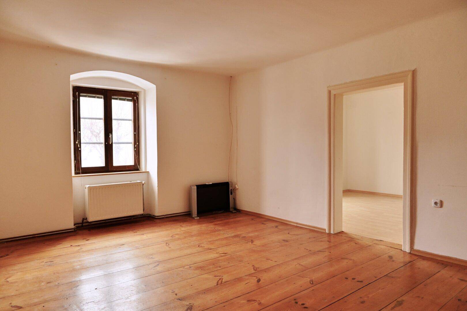 Helles Zimmer mit Holzboden, Fenster und Heizkörper, bietet eine gemütliche Atmosphäre.