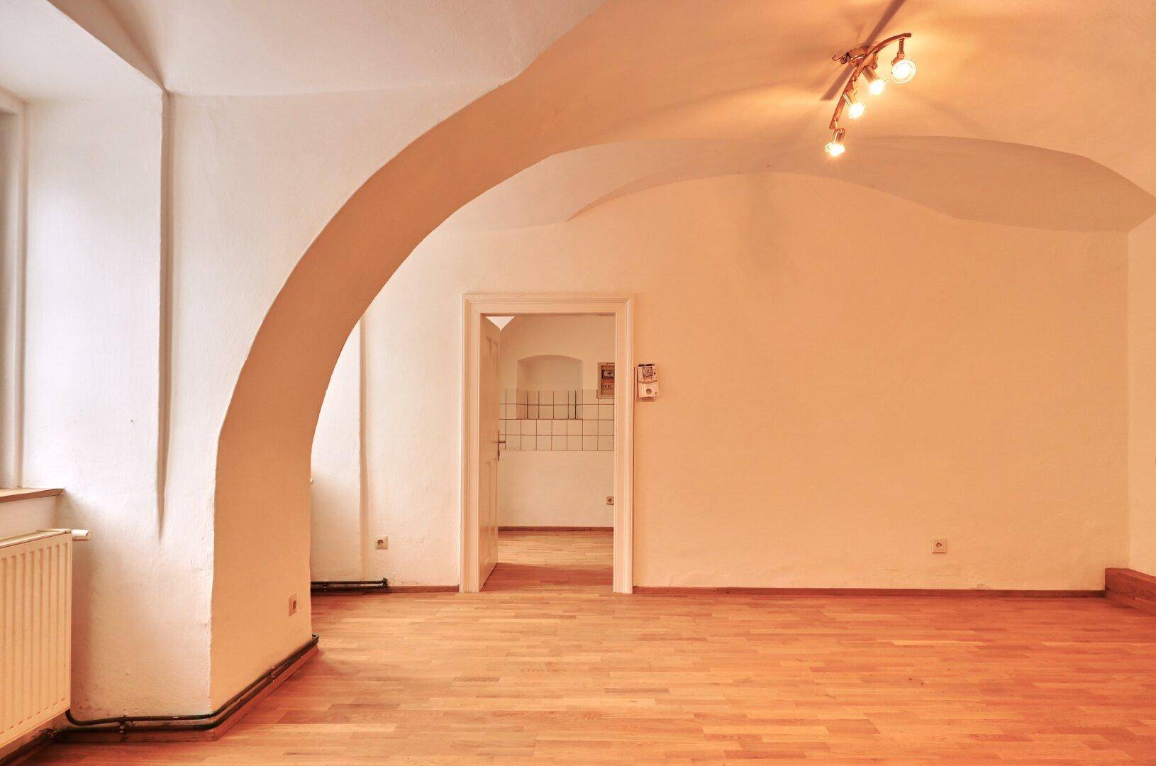 Geräumiger Wohnbereich mit Holzboden, hohen Gewölbedecken und einem dekorativen Bogen.