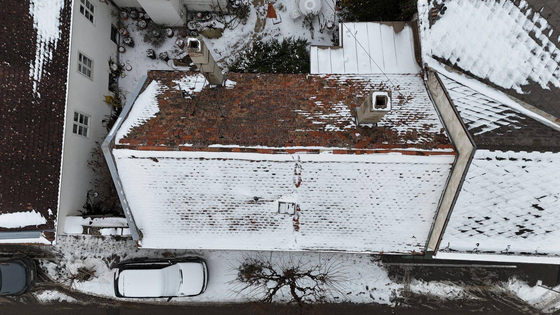 Luftaufnahme eines schneebedeckten Daches und angrenzender Gebäude in einer winterlichen Landschaft.