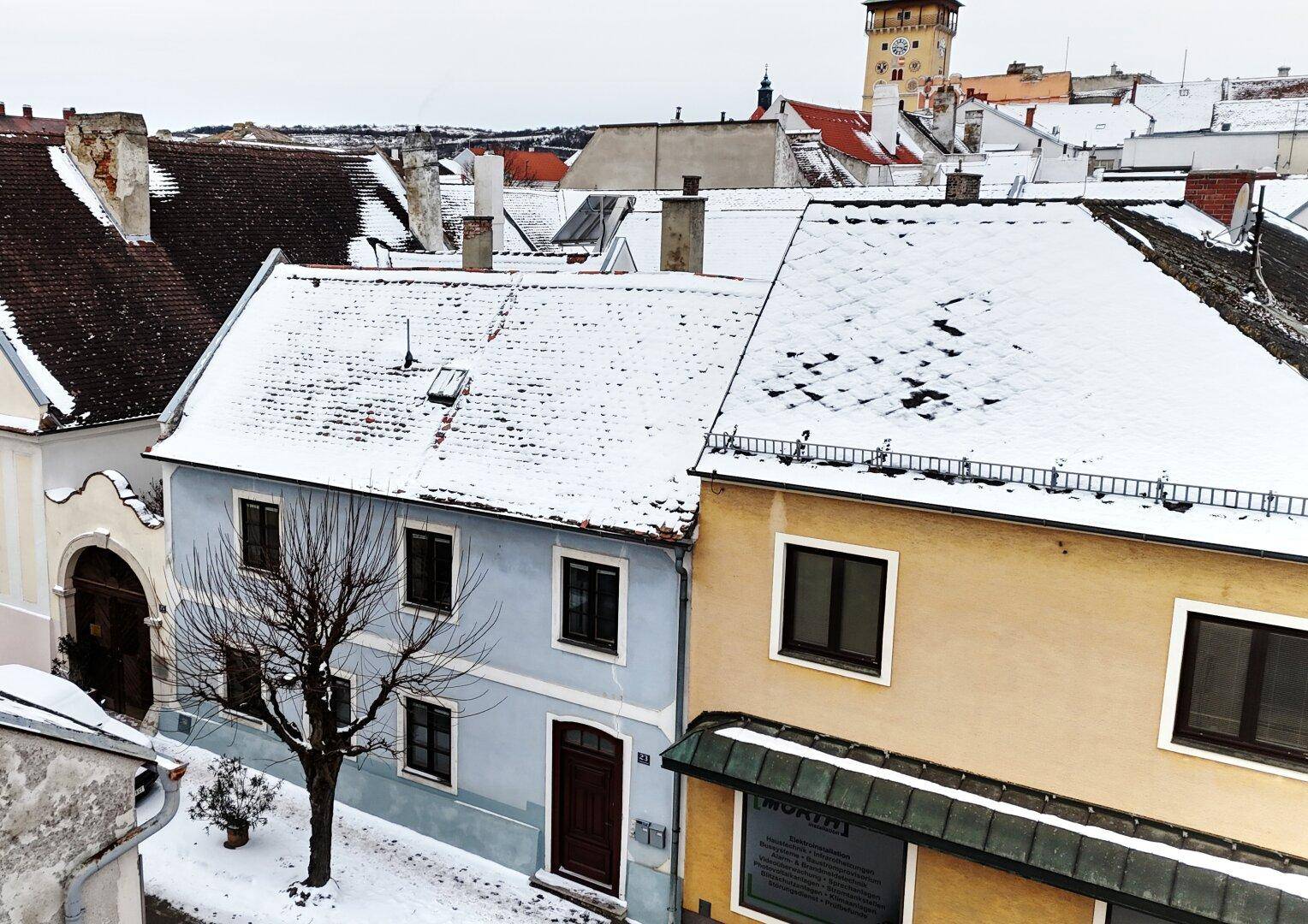 Panoramablick auf eine schneebedeckte Straße mit historischen Häusern und einem Turm im Hintergrund.