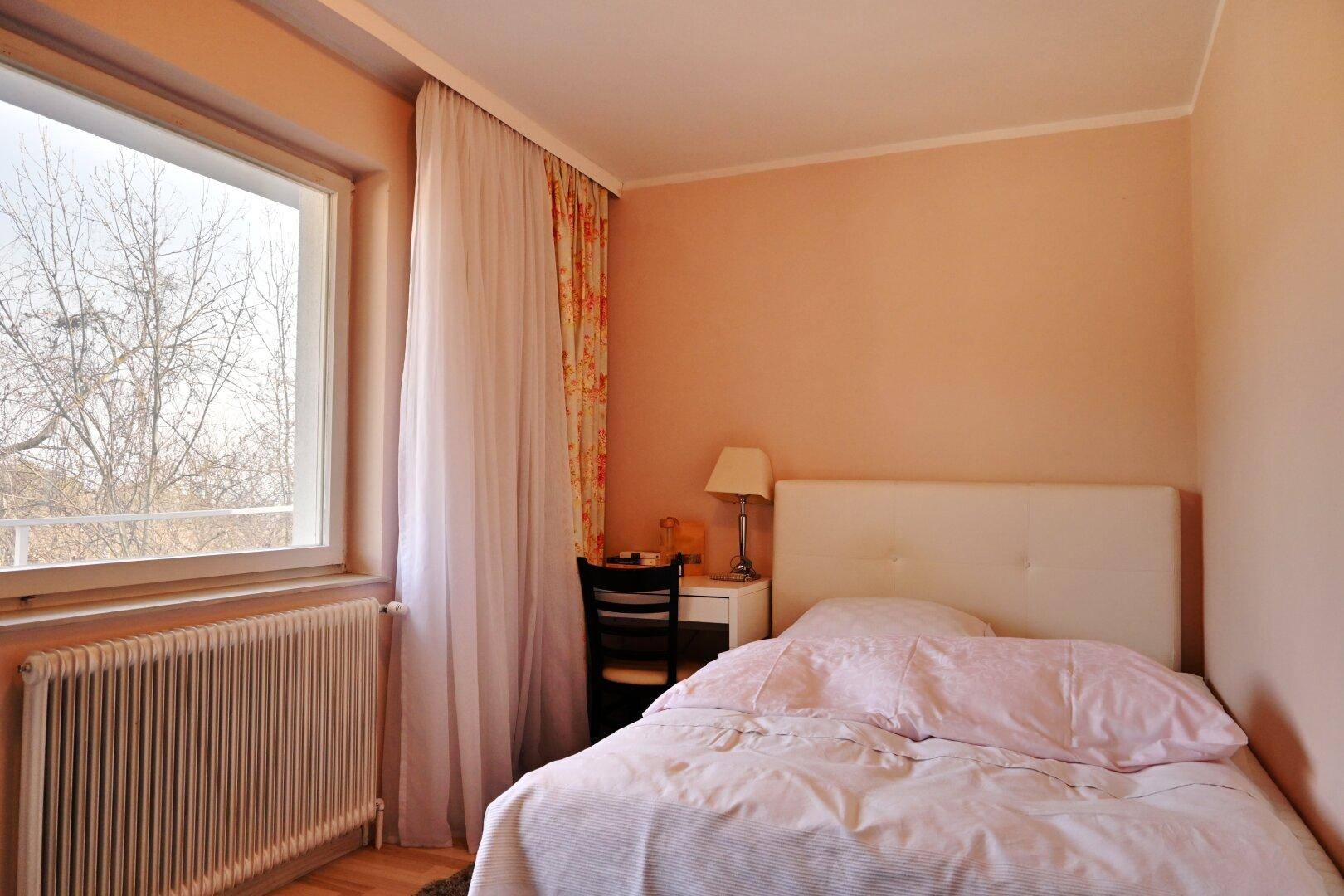 Schlafzimmer mit Einzelbett, rosa Wänden und großem Fenster, hell und freundlich.