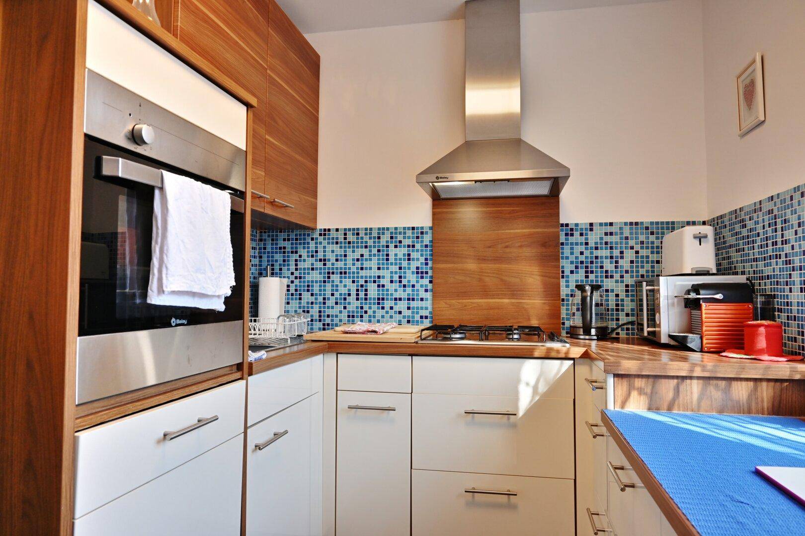 Moderne Küche mit Holzarbeitsplatten, weißen Schränken und blauen Mosaikfliesen.