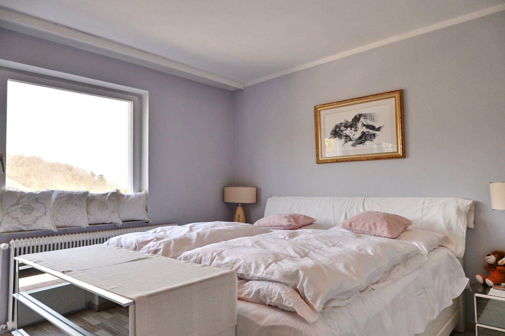 Helles Schlafzimmer mit zwei Einzelbetten, grauen Wänden und großem Fenster.