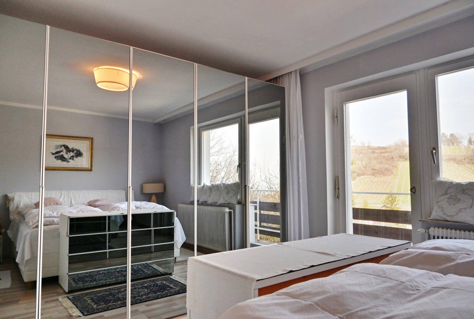 Schlafzimmer mit Spiegelschränken, Doppelbett und Zugang zu einem Balkon.