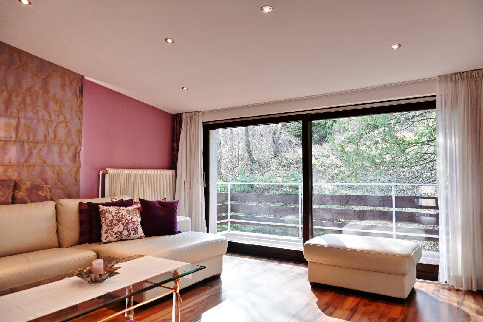Gemütliches Wohnzimmer mit Sofa, Holzboden und großen Fenstern zum Balkon.