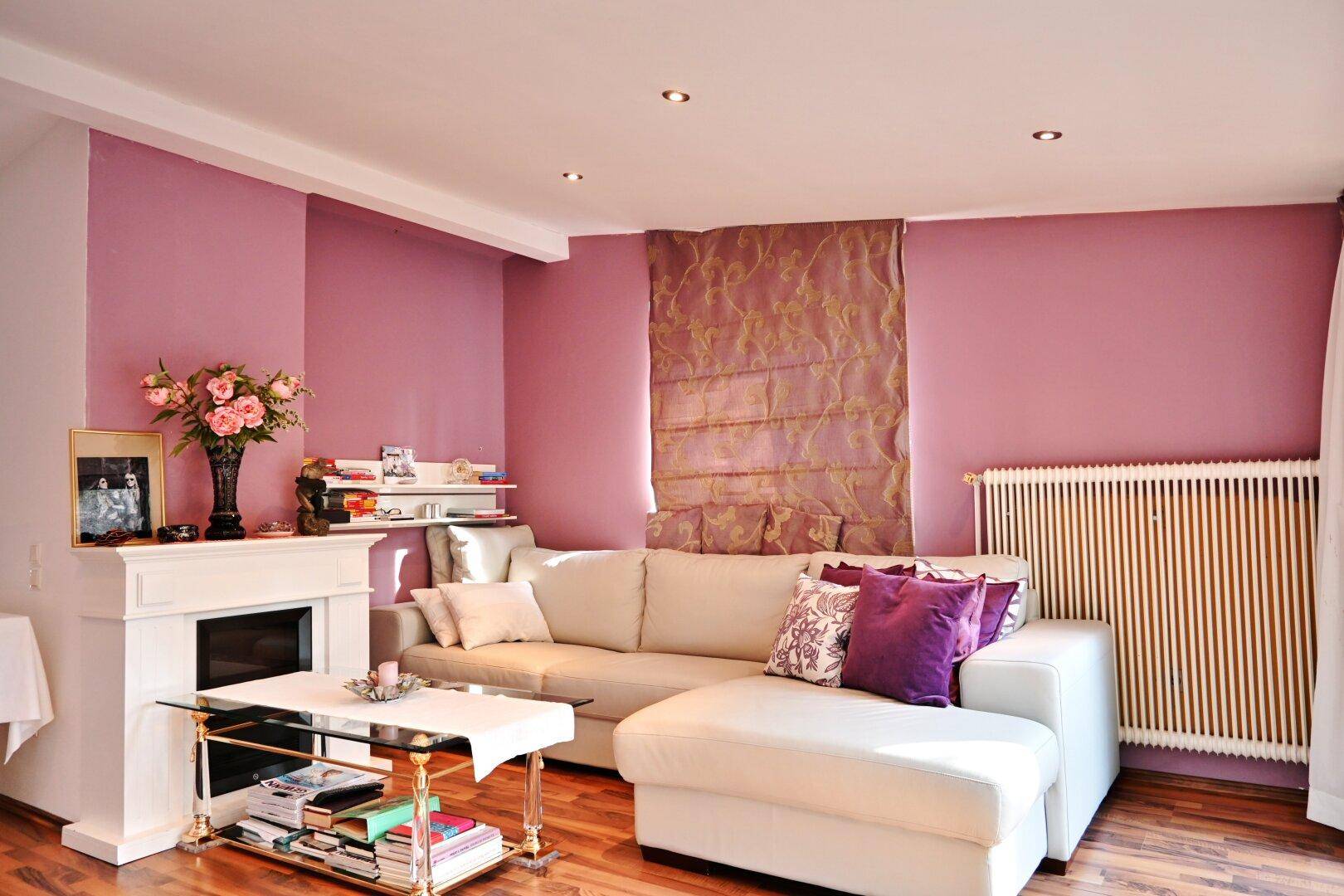 Wohnzimmer mit Kamin, beigem Sofa und rosa Wänden, gemütlich eingerichtet.