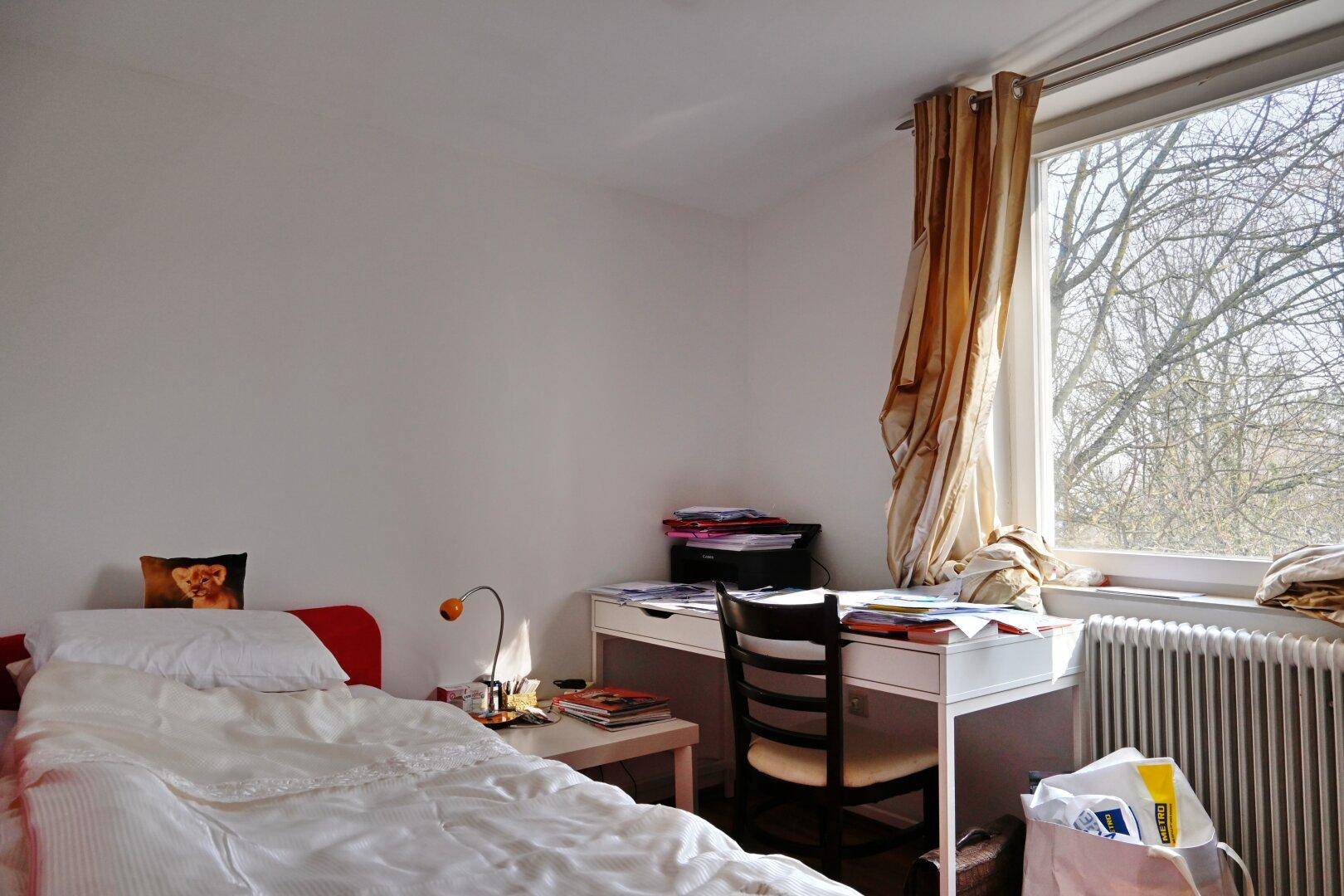 Helles Schlafzimmer mit Einzelbett, Schreibtisch und Fenster mit Blick ins Grüne.