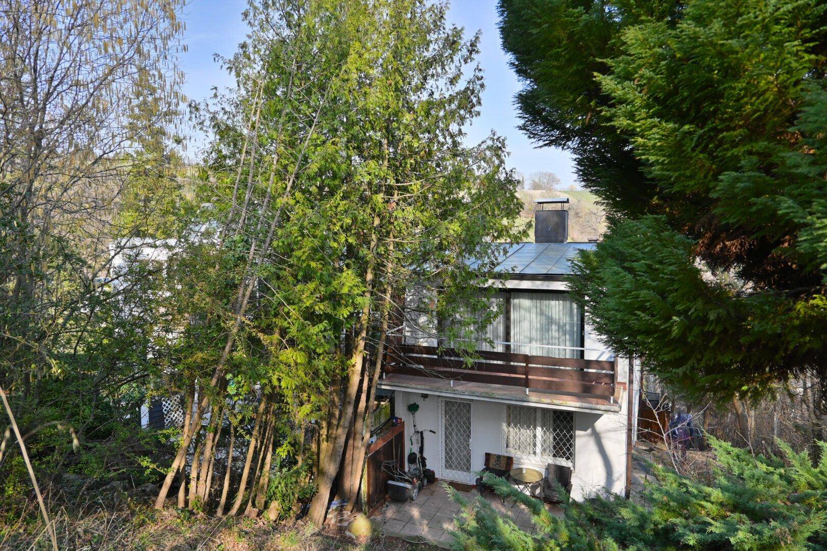 Ansicht des Hauses von außen mit einer kleinen Terrasse und umgebenden Bäumen.