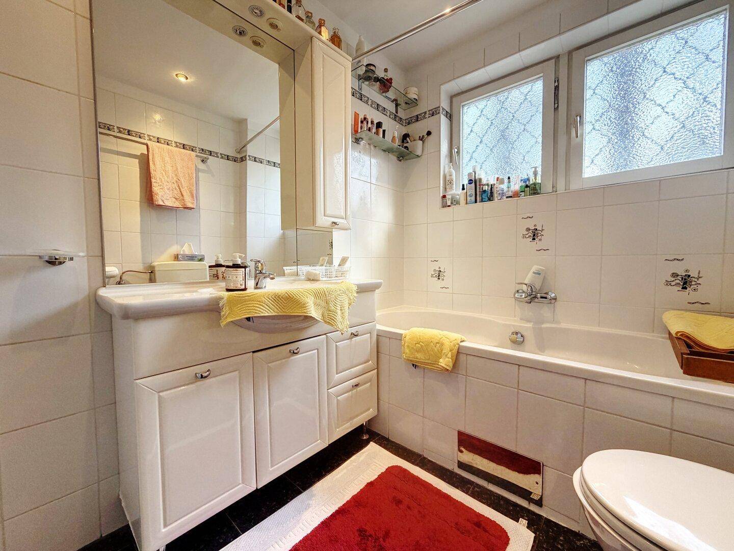 Badezimmer mit Badewanne, Waschbecken und Fenster, in weiß gefliest.