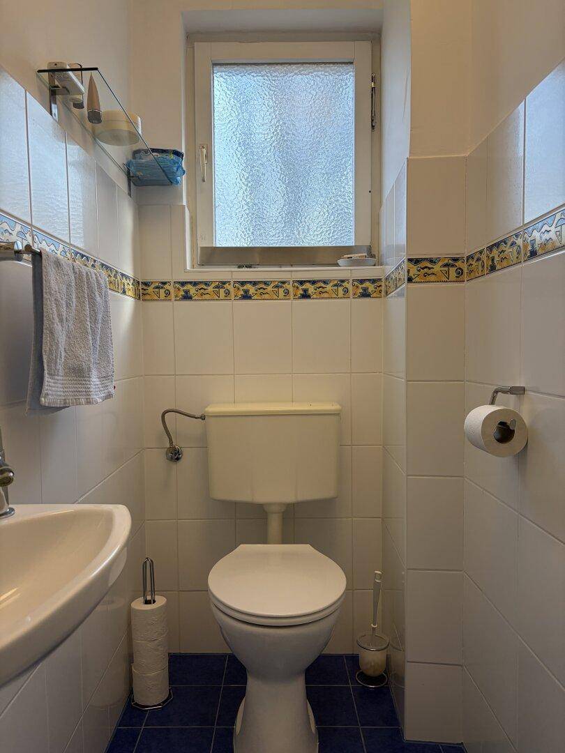 Kleines Gäste-WC mit Fenster, Toilette und Waschbecken, in hellen Fliesen gehalten.