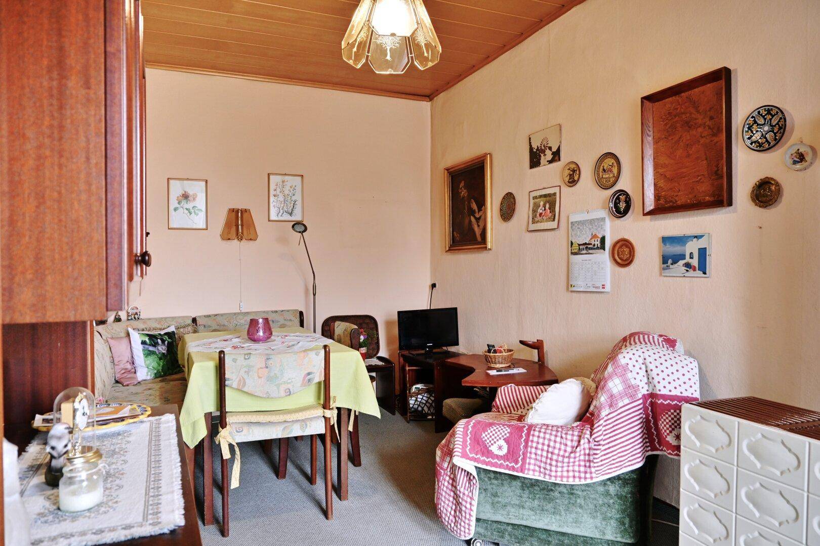 Wohnraum mit Holztäfelung, vielen Bildern an der Wand und einem Kachelofen.