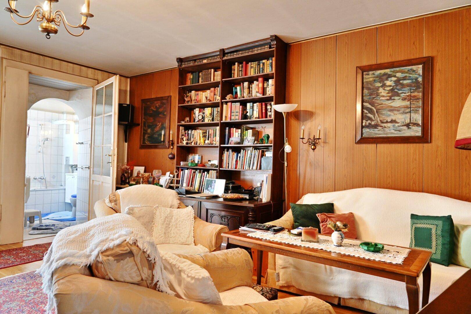 Wohnzimmer mit Holztäfelung, großem Bücherregal und bequemen Sesseln.