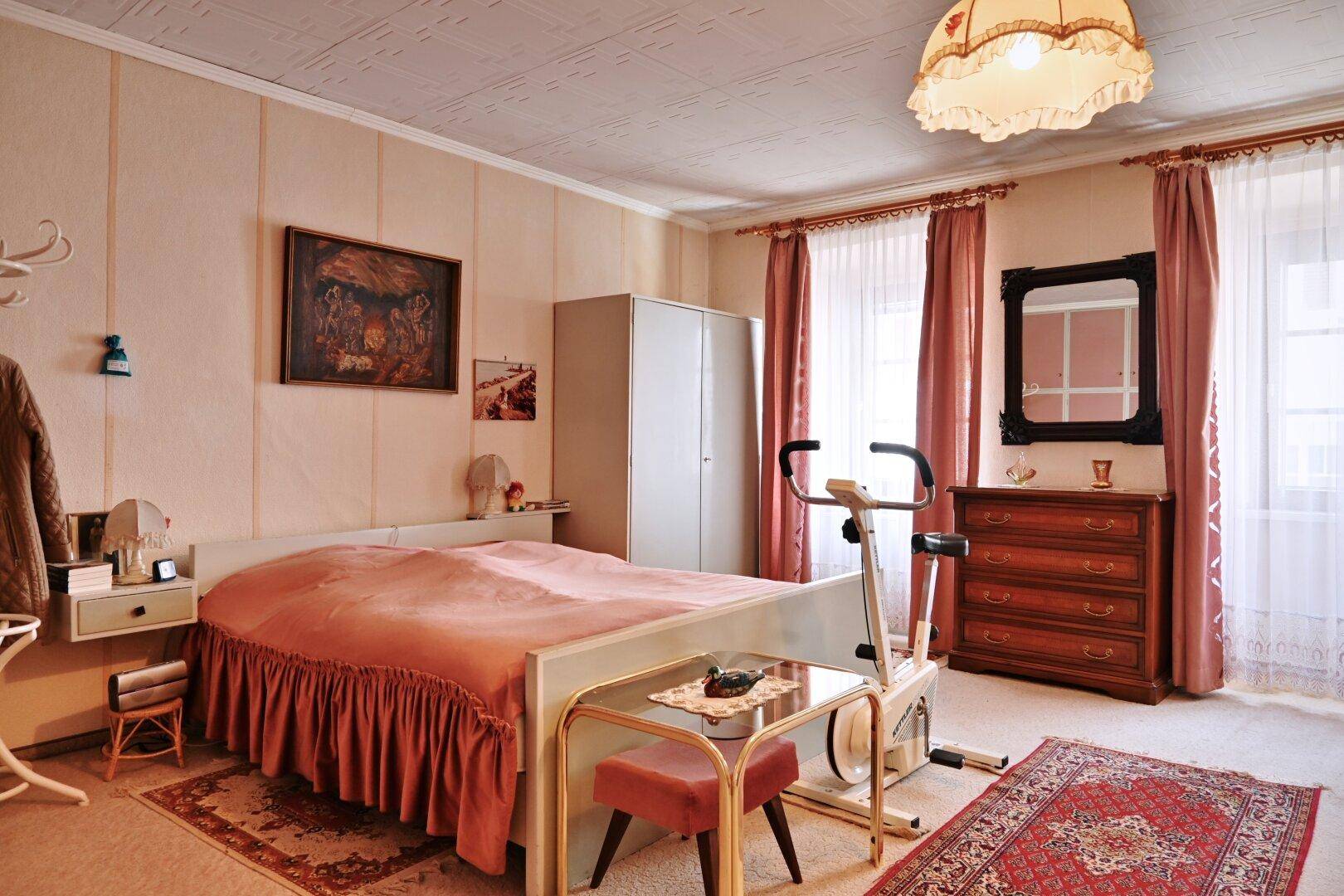 Schlafzimmer mit Doppelbett, rosa Vorhängen und einem Heimtrainer für sportliche Aktivitäten.