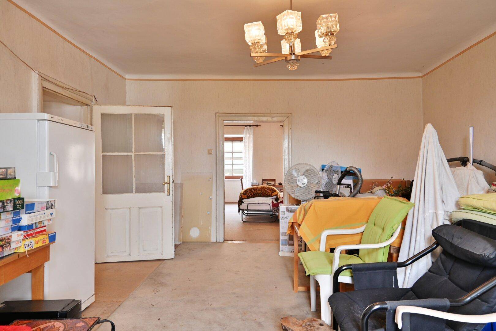 Großer, unmöblierter Raum mit Kühlschrank und Blick in einen weiteren Raum.