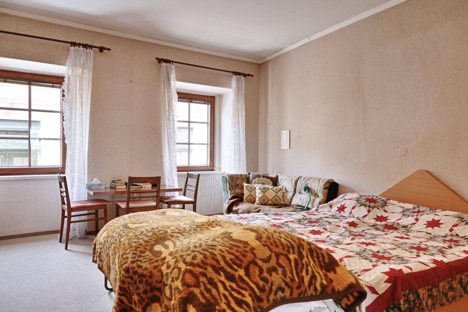 Schlafzimmer mit zwei Betten, einem kleinen Tisch und Blick auf die Straße.