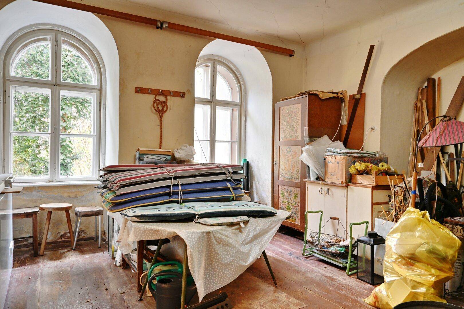 Geräumiger Raum mit großen Rundbogenfenstern und vielen gelagerten Gegenständen.