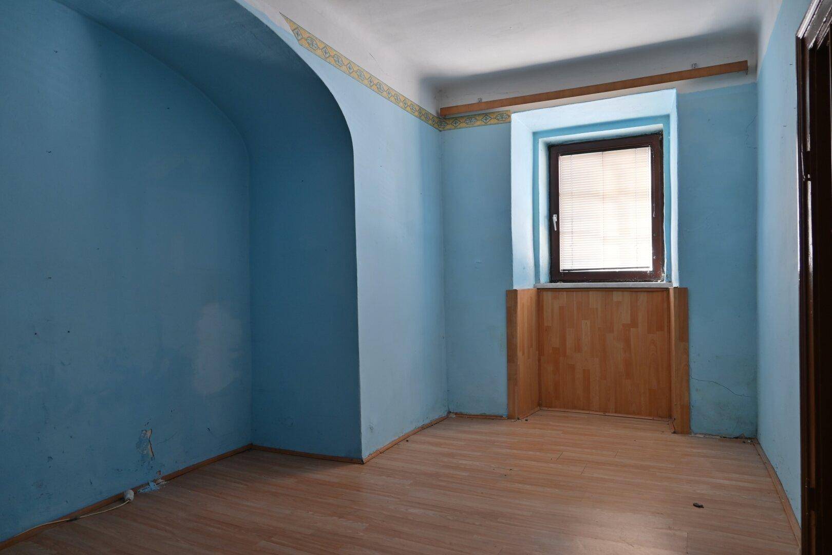 Kleiner Raum mit blauen Wänden, Holzboden und einem Fenster mit Holzverkleidung.