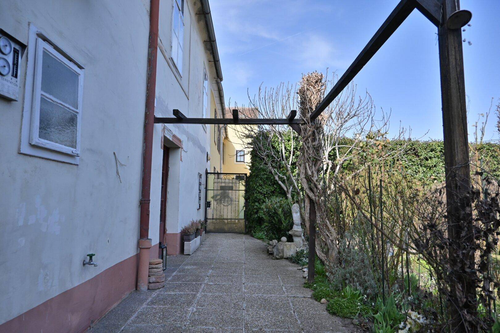 Gepflasterter Weg entlang der Hauswand mit einem Tor zum Gartenbereich.