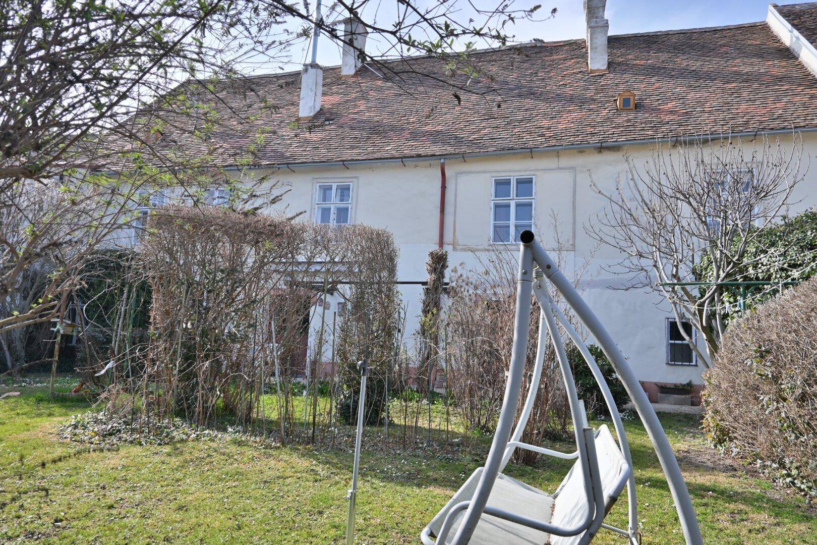 Gartenansicht mit Schaukel im Vordergrund und der Rückseite des Hauses im Hintergrund.