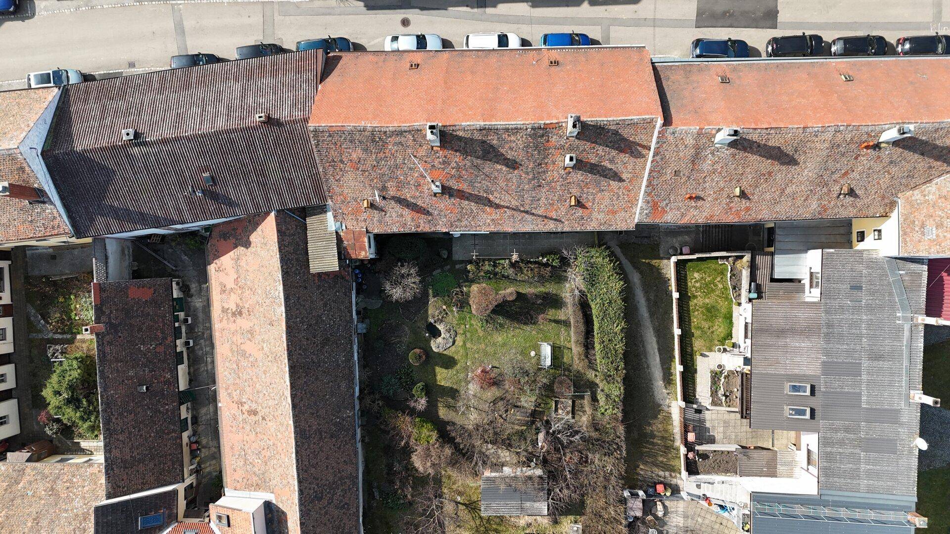 Draufsicht auf die Dächer der Gebäude und den dahinterliegenden Gartenbereich.