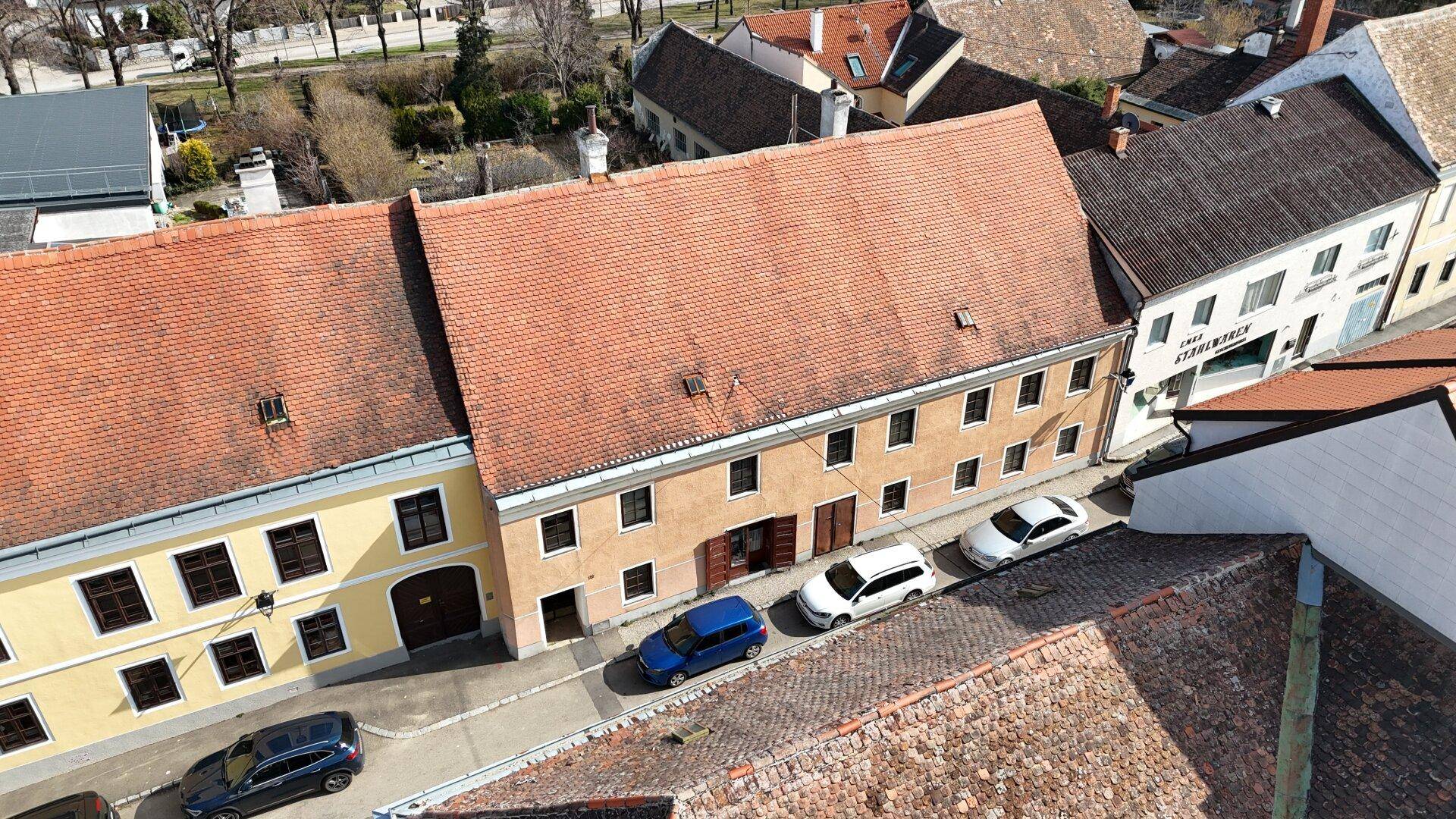 Luftaufnahme einer Straße mit parkenden Autos und historischen Gebäudefassaden.