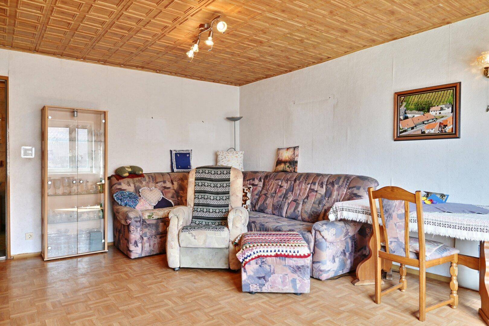 Gemütliches Wohnzimmer mit Sofa, Vitrine und Parkettboden unter Holzdecke.