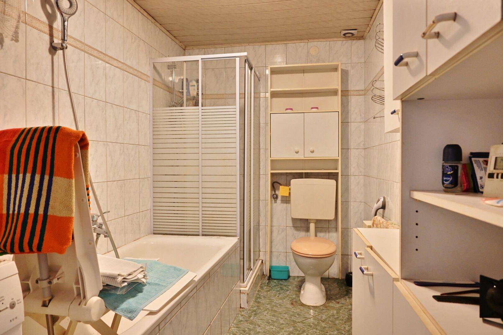 Funktionales Badezimmer mit Badewanne, Duschkabine und Fliesen an Wänden und Boden.