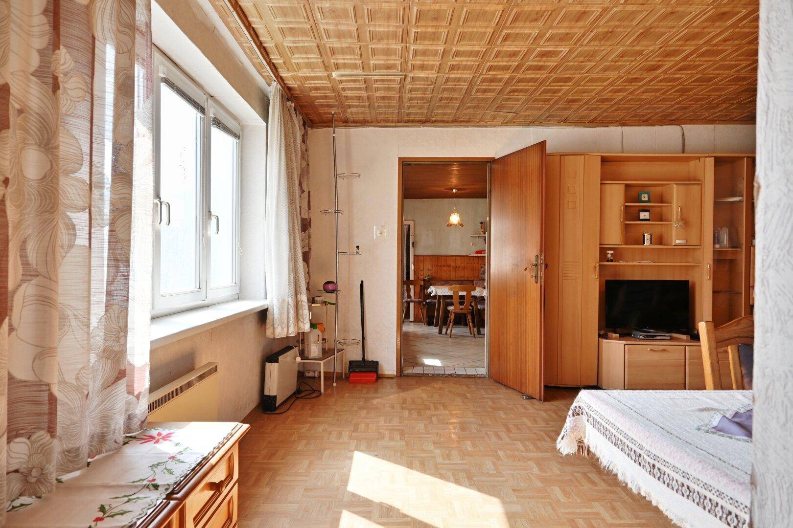 Wohnzimmer mit Parkettboden, großen Fenstern und Blick in den Essbereich.
