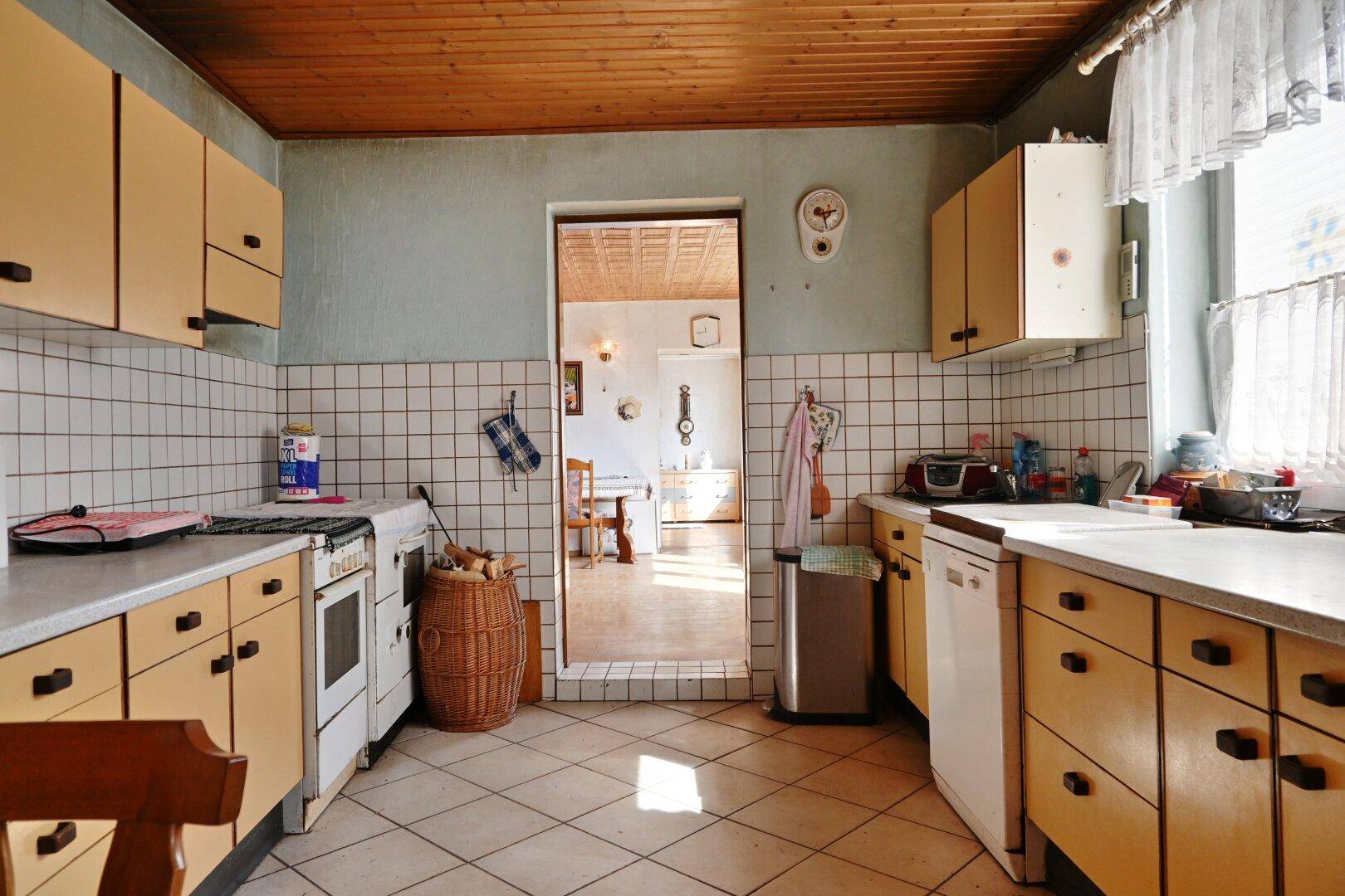 Traditionelle Küche mit hellen Schränken, Fliesenboden und Blick in den Essbereich.