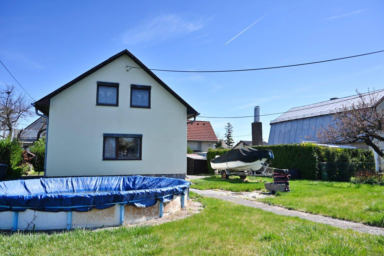 Einfamilienhaus mit Garten, Rasenfläche und einem Aufstellpool unter blauem Himmel.